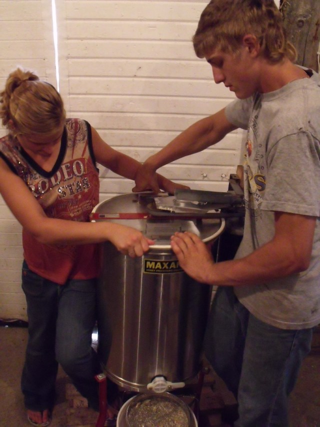 Maggie and Caleb steady and operate the honey extractor.  